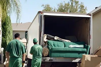 Two movers loading an old sofa and boxes into a junk removal truck